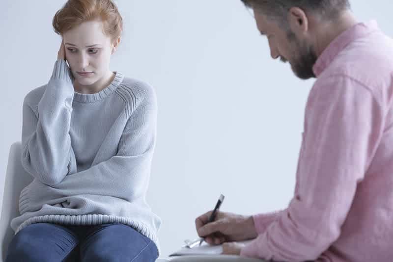 distraught woman turning away as therapist asks her about the seven facts about addiction treatment that people don't understand