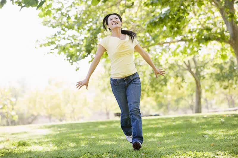 woman in yellow shirt running happily in a park illustrating how to live a life free of bad habits