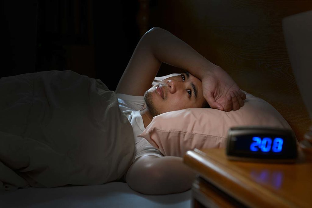man lying awake in bed at 2:08 AM illustrating alcohol withdrawal symptoms