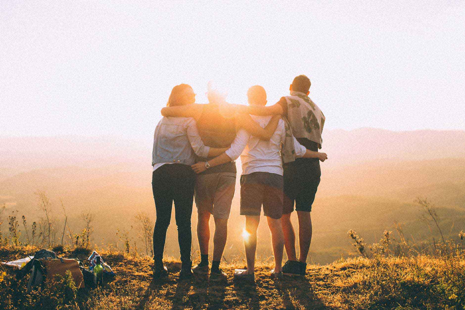 four friends arm in arm on hill overlooking sunset