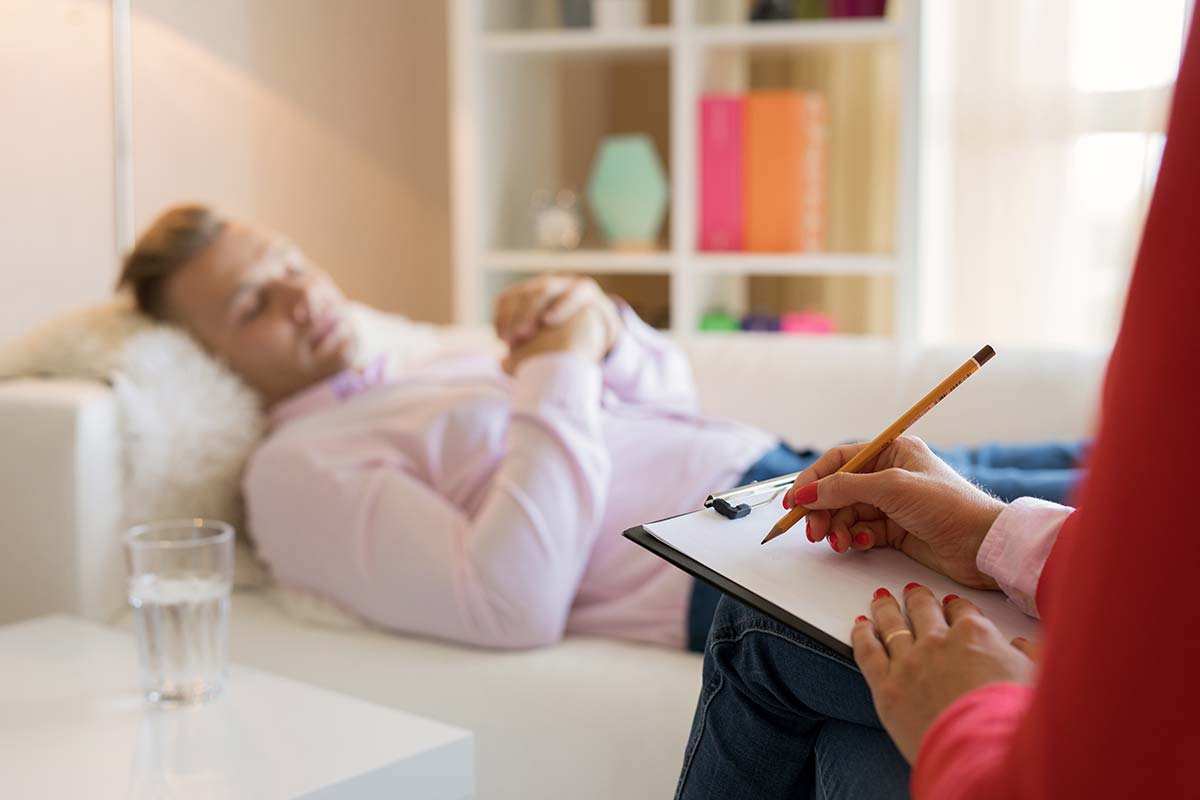 man sleeping on therapy couch with therapist present wondering how does hypnotherapy work