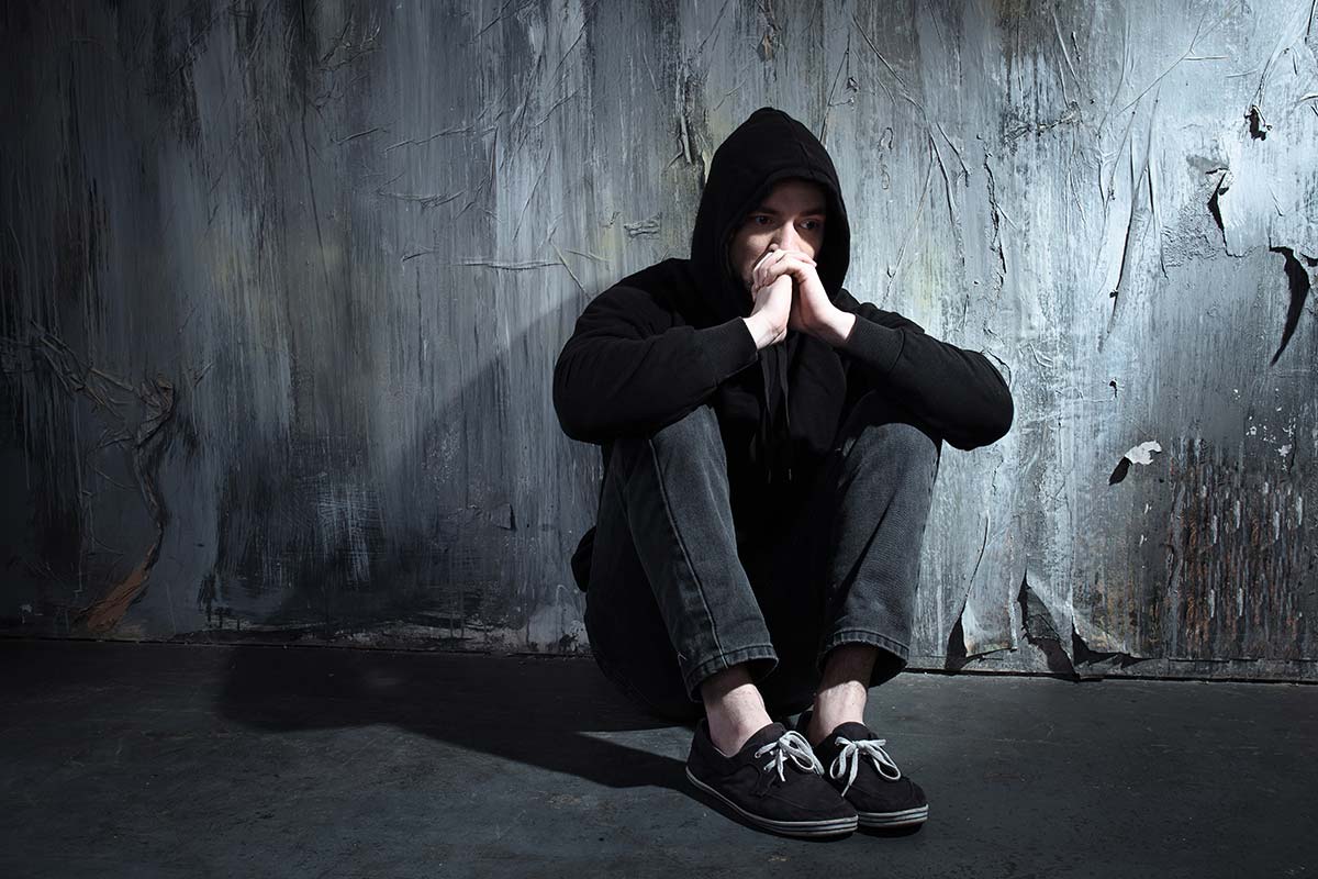 man in hoodie slumped against squalid wall wondering is addiction a disease