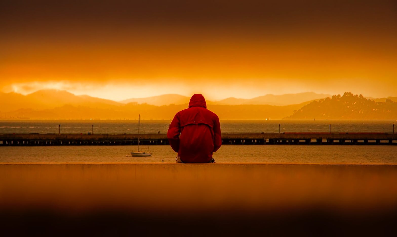 rear view of person in hooded jacket overlooking the sea at sunrise illustrating suicide and self harm with addiction